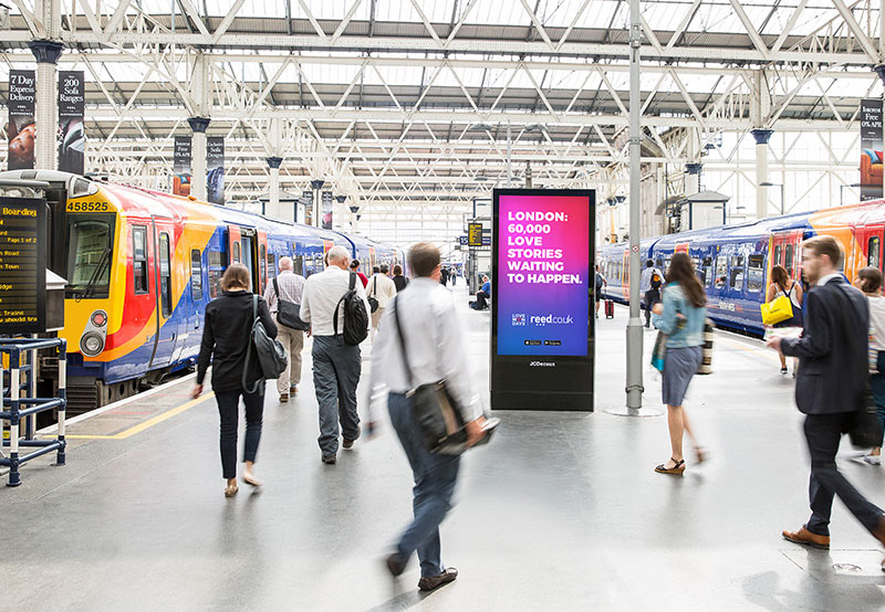 Love Mondays poster beside trains in a busy station