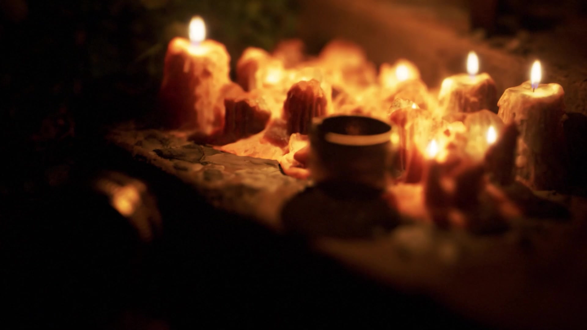 Close-up of melted candles and a small vessel lit by warm flames